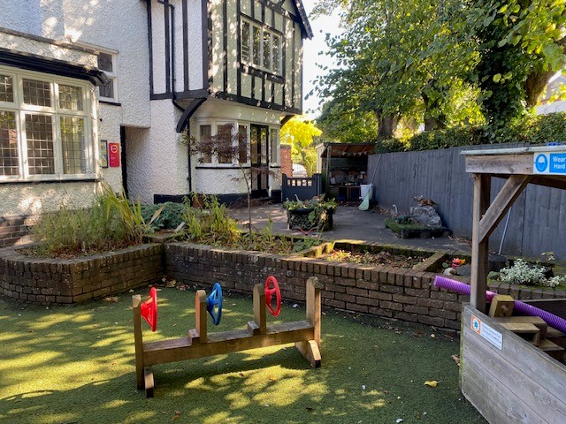 Outdoor space with grass, wooden hut and wheels at Partou Day Nursery & Pre-School in West Bridgford