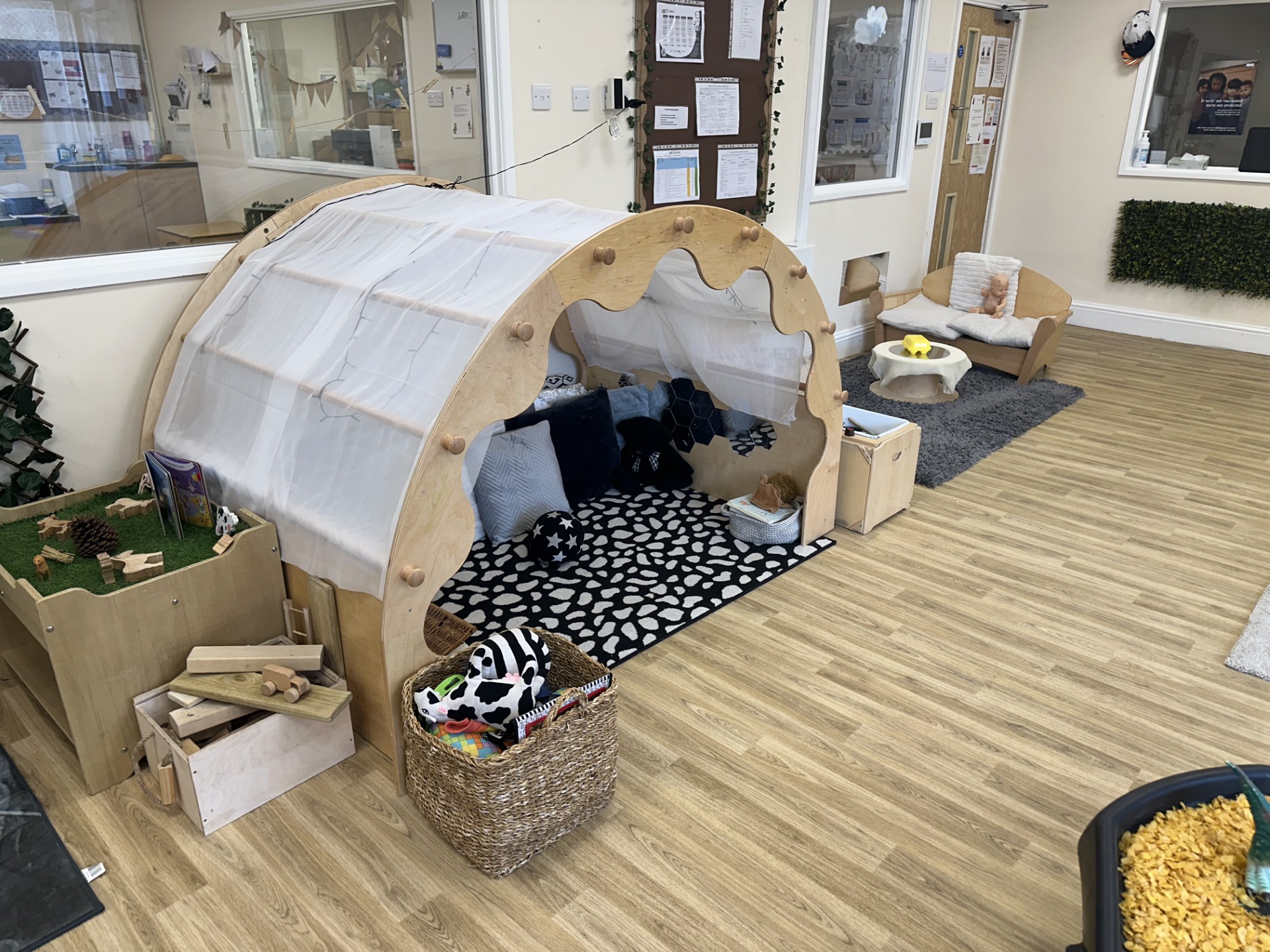 Small wooden sheltered area with carpet and cushions for reading and relaxing at Partou Upton Day Nursery