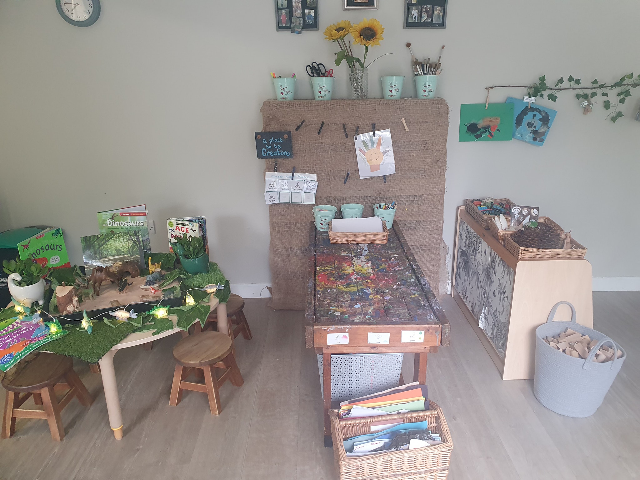Dinosaur books and toys on a table next to a painting bench in the creativity corner at Partou Scotts Wood Day Nursery in West Bridgford