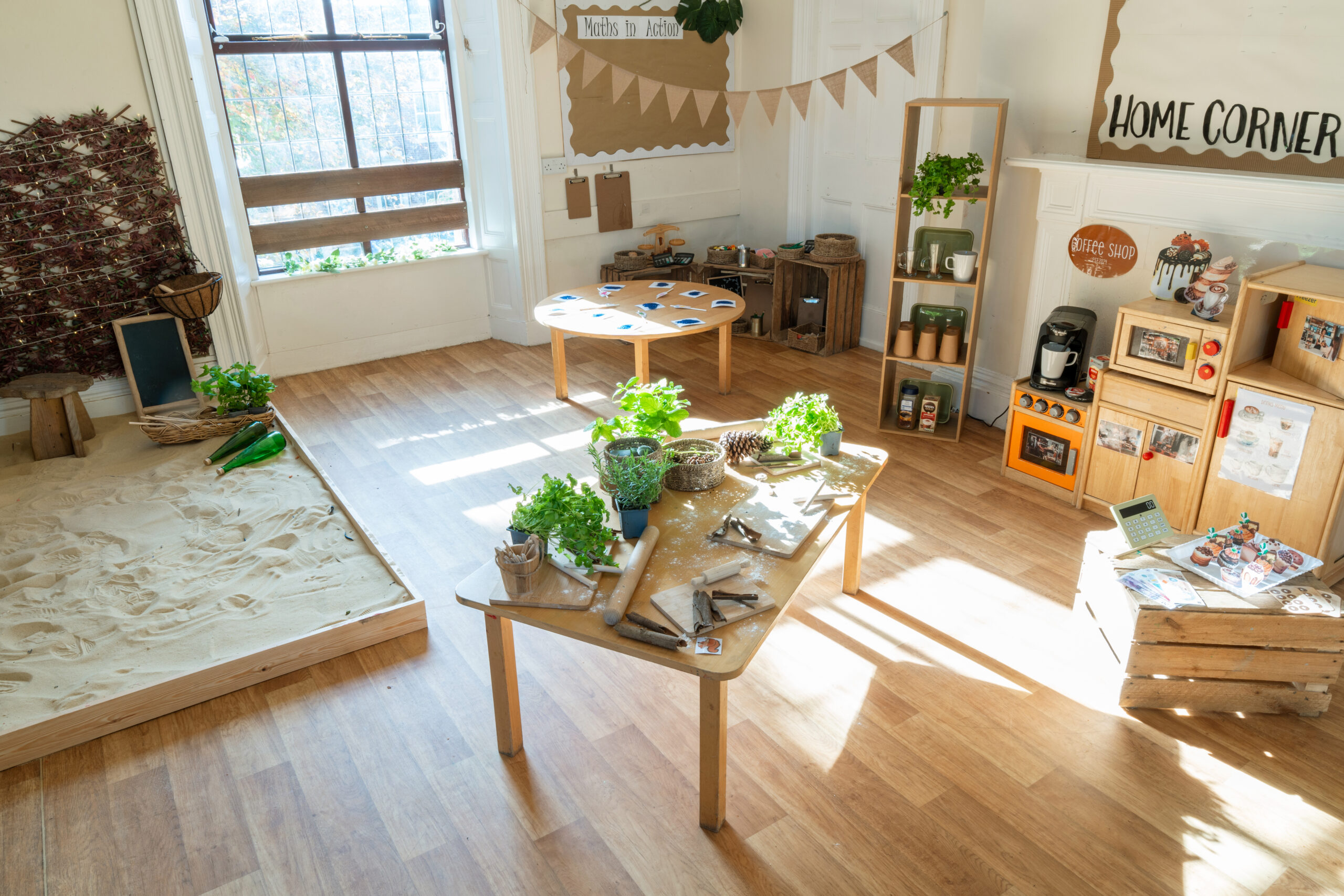 Home from home toddler area with wooden cupboards, oven and microwave next to a snadpit and table at Hilltops nursery in Chorley