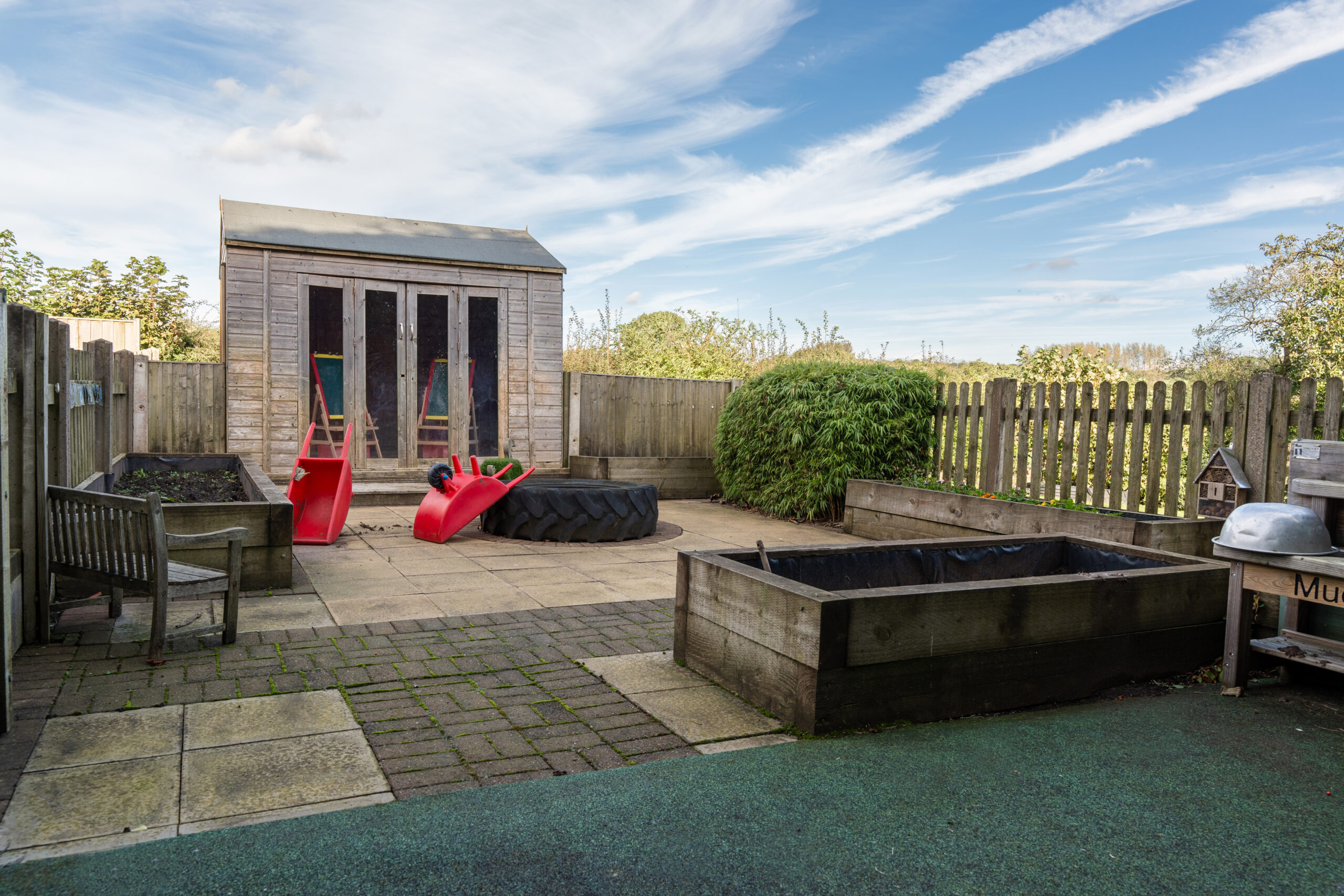 Outdoor play area at Hilltops nursery in Chorley with wooden shed, sandpit, mud kitchen and small wheel barrows