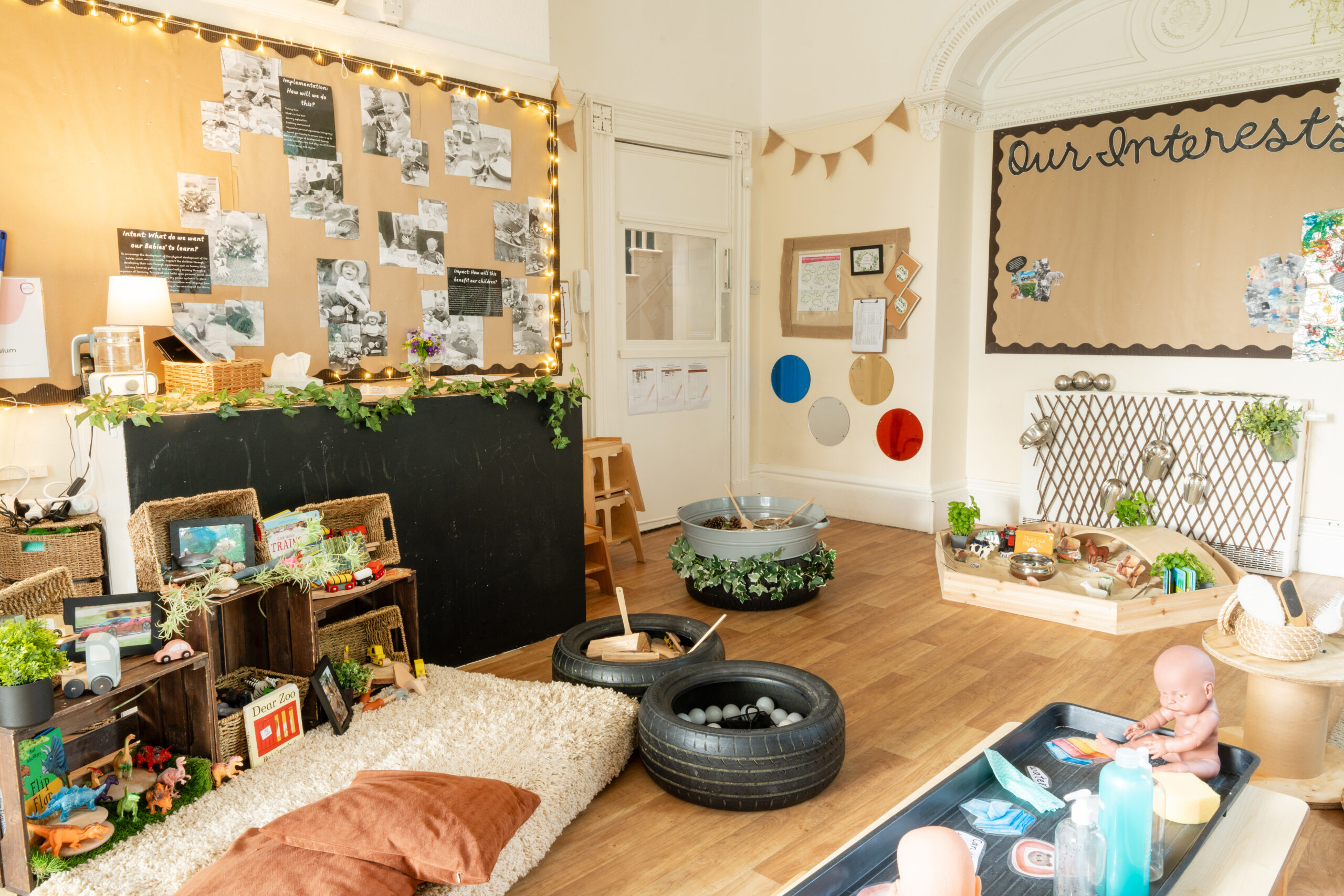 Toddler room with pretend baby care station, reading area, sandpit and wall displays at Hilltops nursery in Chorley