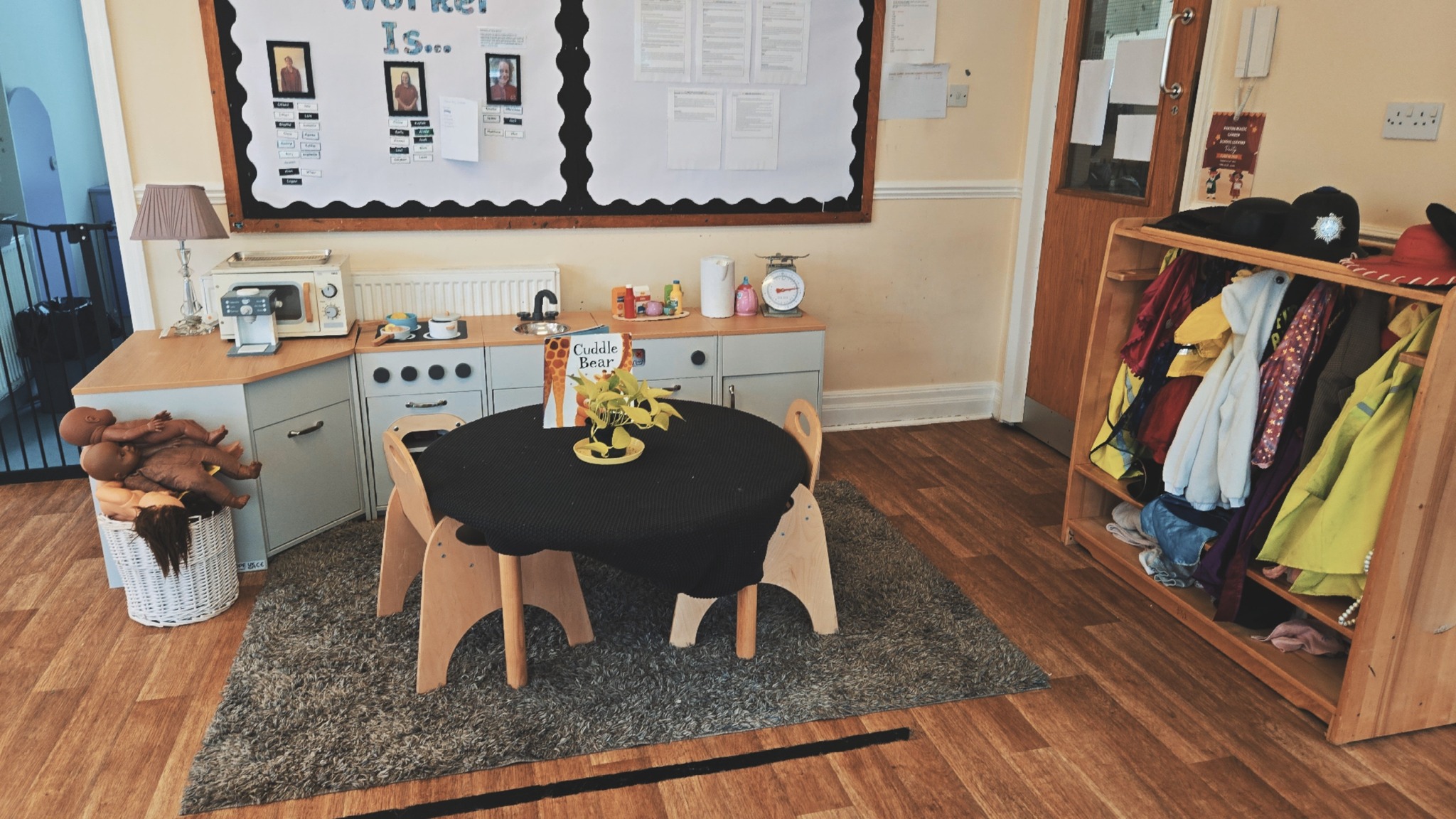 Small wooden table and chairs next to wooden play kitchen near various dressing up clothes at Partou Magiv Garden day nursery and pre-school in Moortown, Leeds