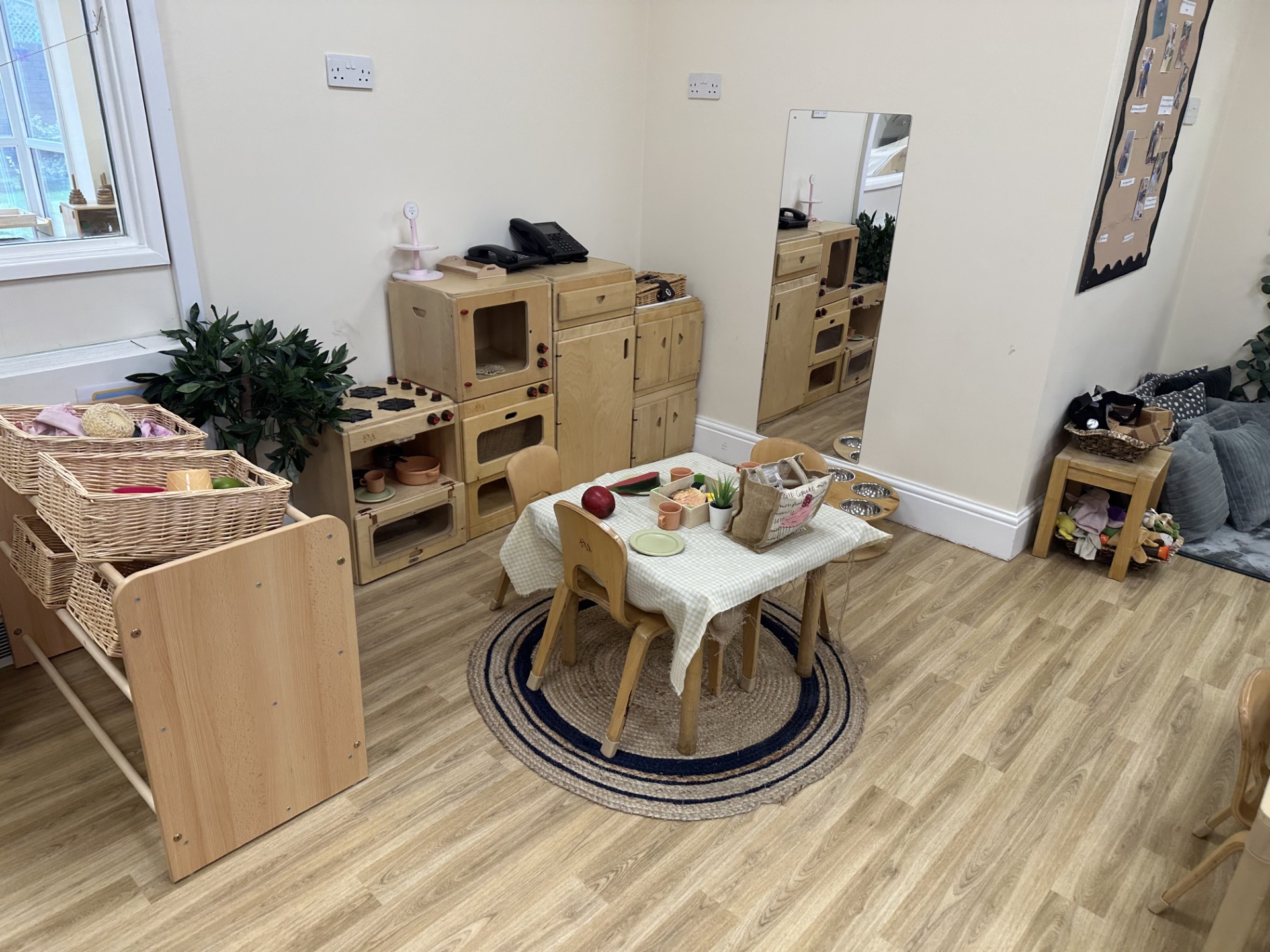 Wooden kitchen role play toys with dollies at a wooden table and chairs at Partou Upton Day Nutrsery in Prenton