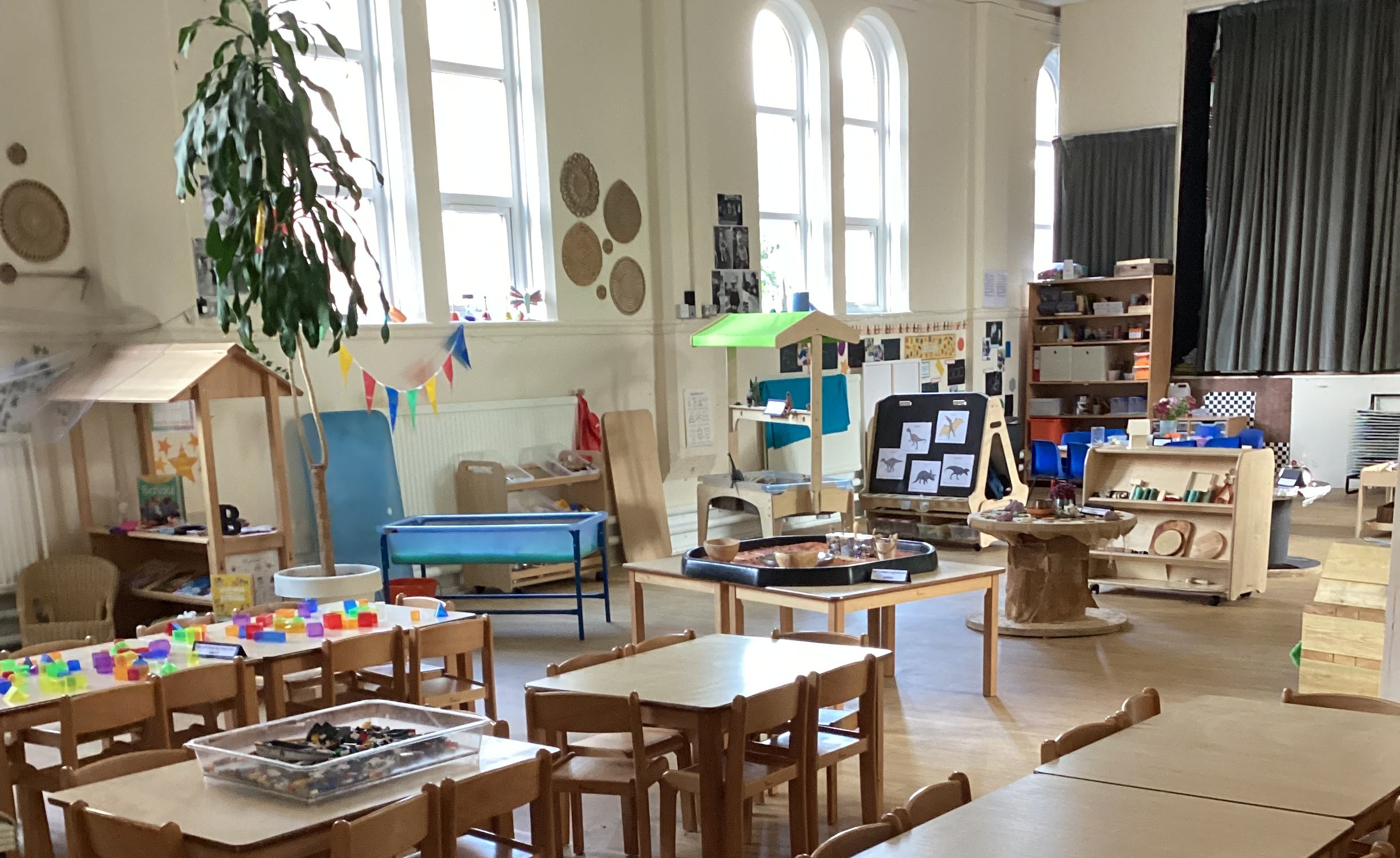Large and bright hall with stage and tables and chairs set up with various sensory play activities set up at Partou Footrpints nursery
