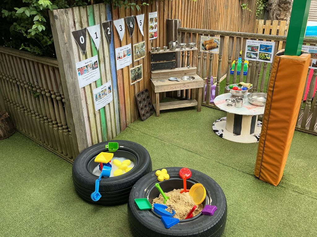 Green AstroTurf with two tyres containing sand and water for sensory play at Partou Acorns in Adel nursery and pre-school in Leeds