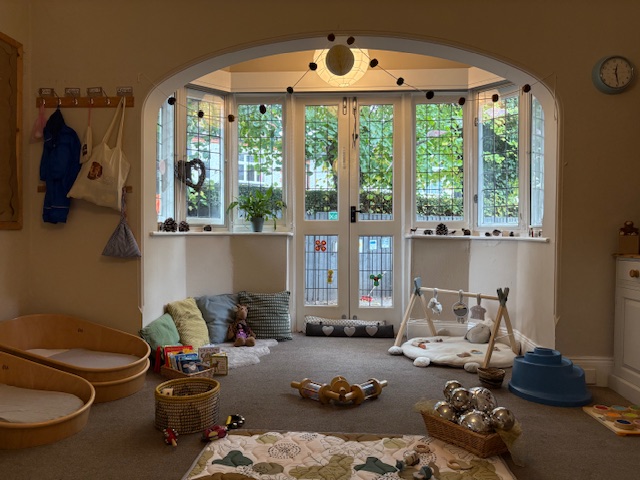 Carpeted area with large windows and patio door, sleeping cots and sensory toys for babies at Partou Leo