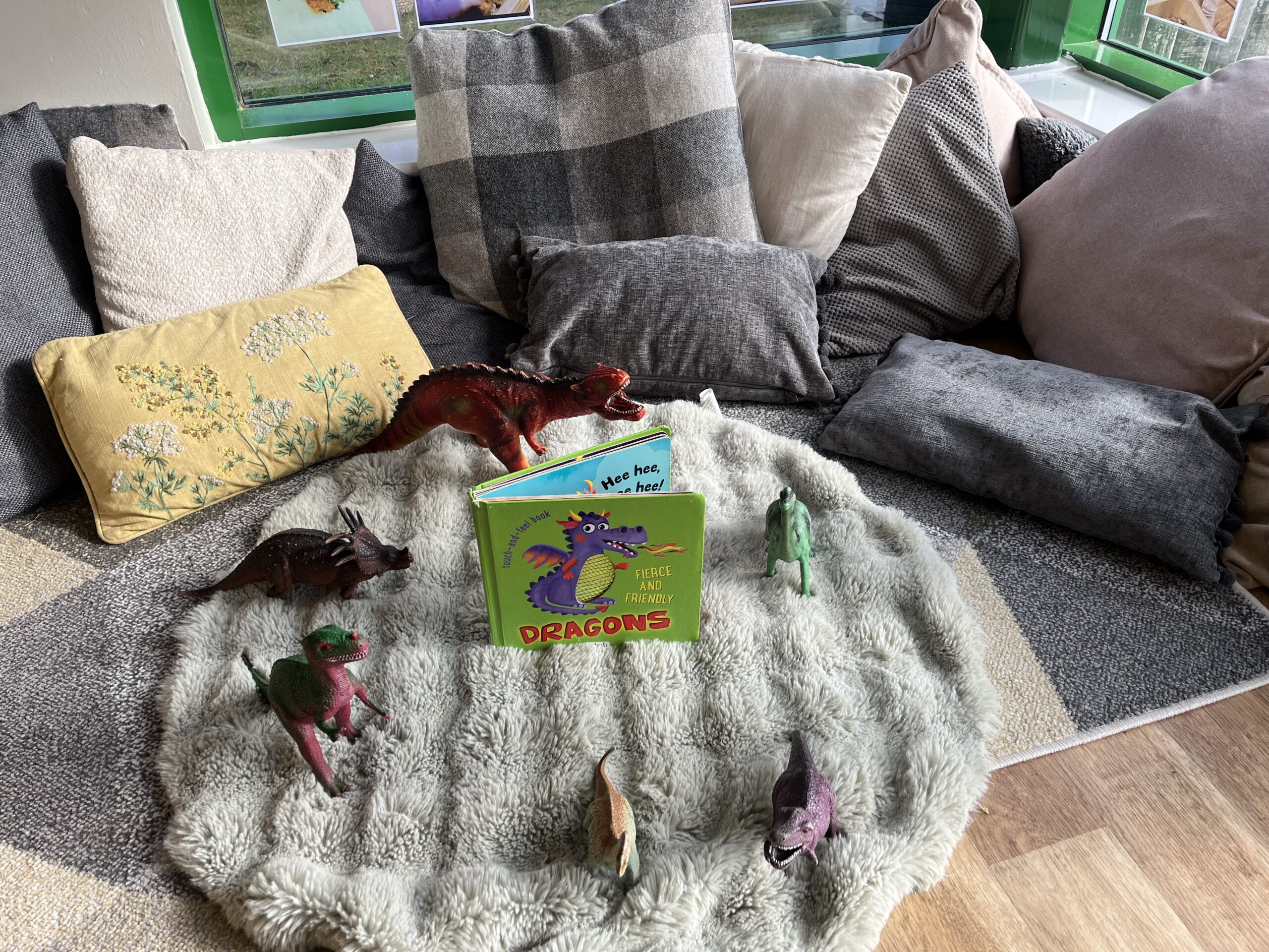 Fluffy rug surrounded by cushions of various sizes with dinosaur book and toys at Partou Smileys nursery in Stafford