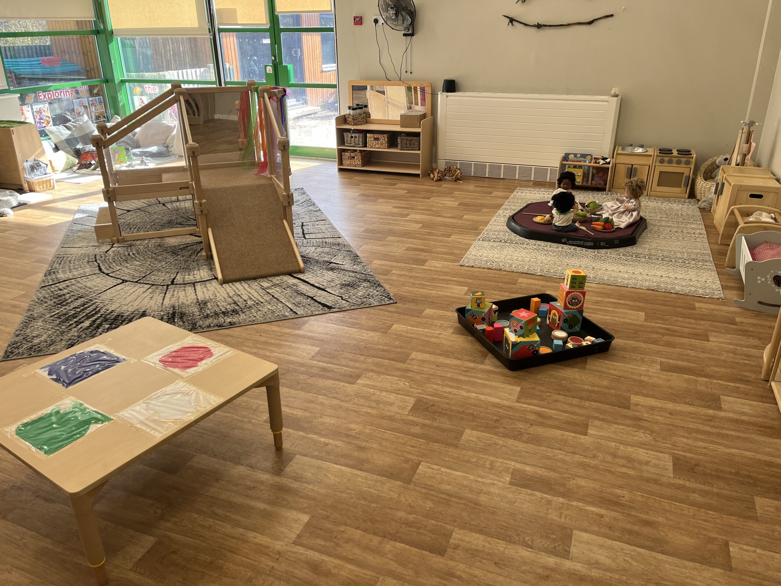 Wooden toddler play frame next to painting and sensory activities at Partou Smileys nursery in Stafford