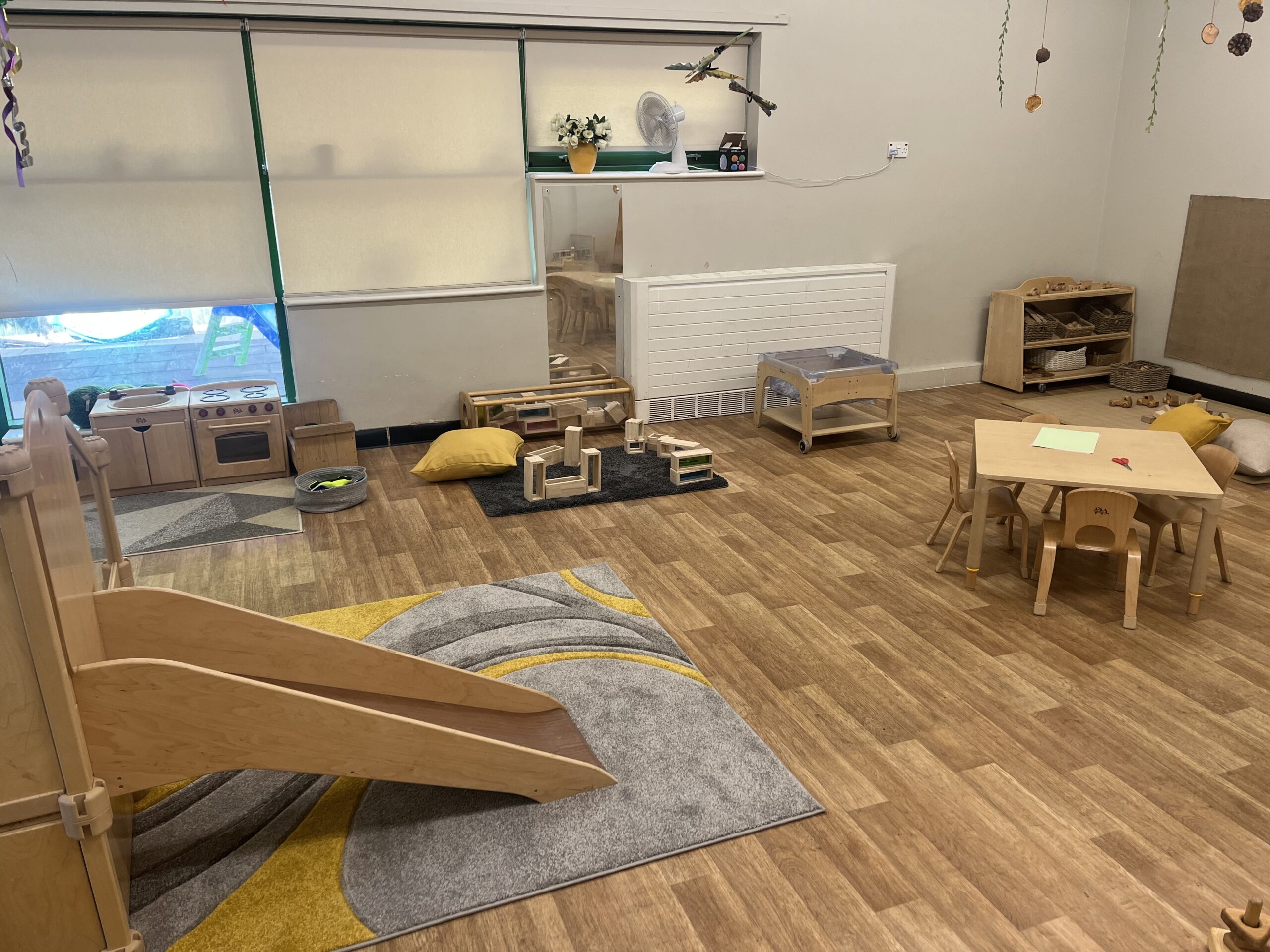 Wooden toys and frame on a grey and mustrad rug in the baby room at Partou Smileys nursery in Stafford