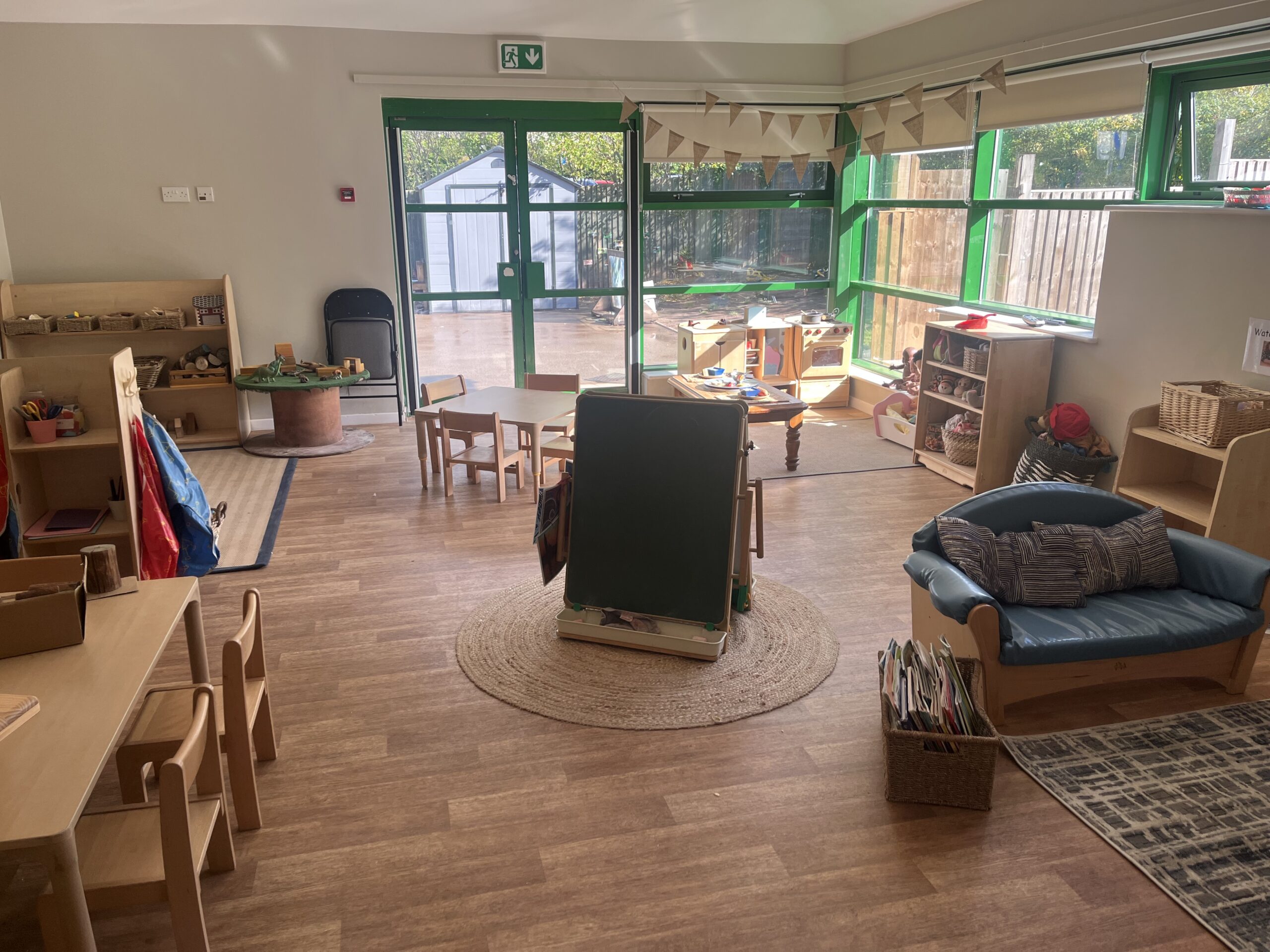 Large wooden floored toddler room with large windows and light streaming in on children