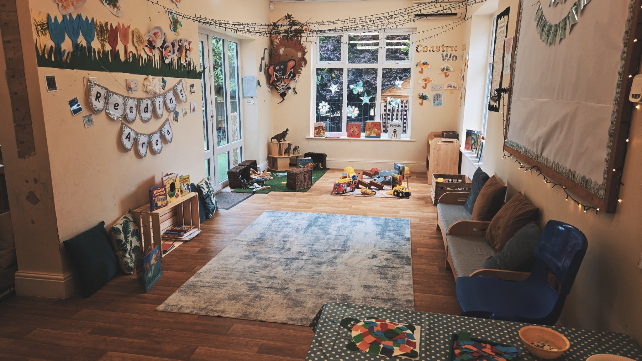 Reading area with rug, chairs and books near to construction and dinosaur toys at Partou Magic Garden nursery in Leeds