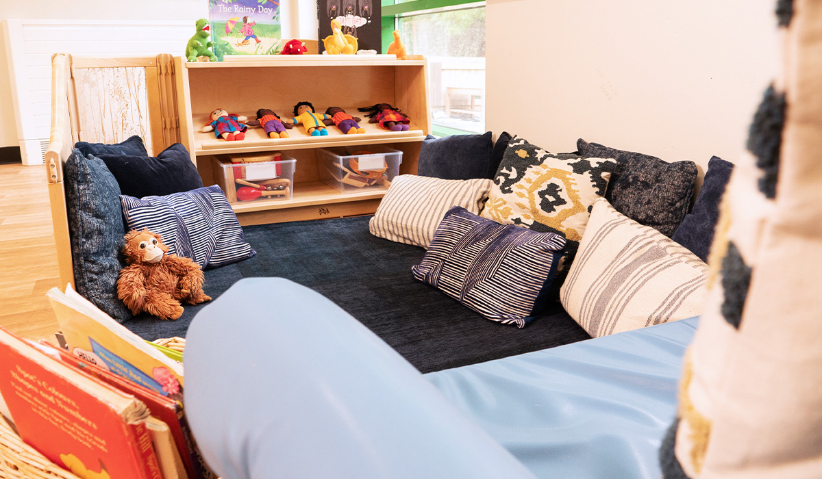 Cozy blue carpeted area with cushions, books and soft dolls at Smileys nursery in Stafford