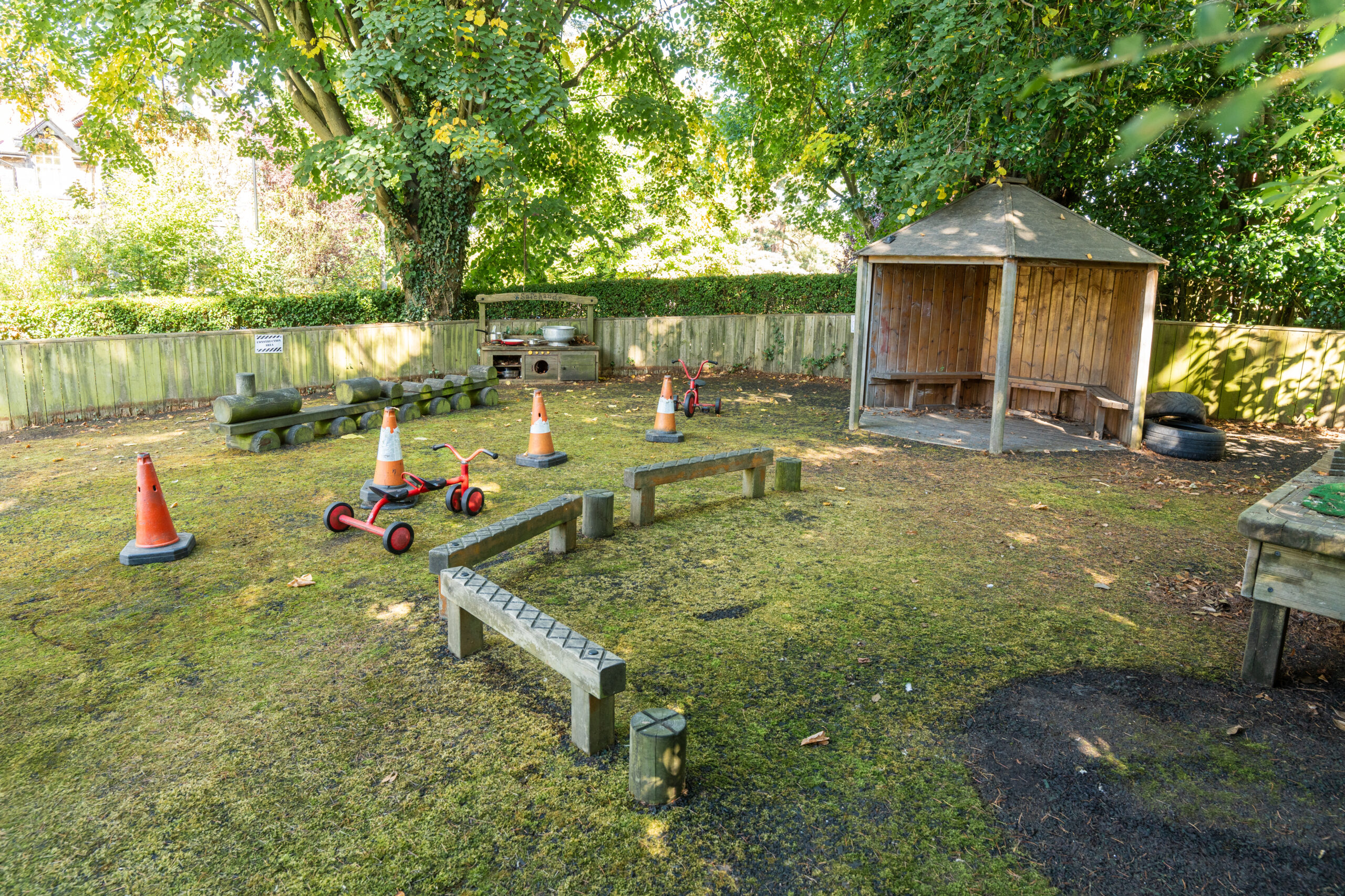 Outdoor area at Safehands nursery in Harrogate with balance beams and bikes and wooden hut with benches
