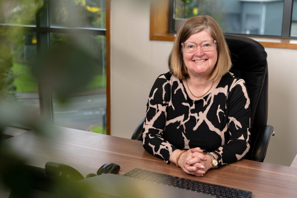 Samantha Rhodes, Managing Director of Partou, sits at a desk in an office setting, smiling towards the camera.