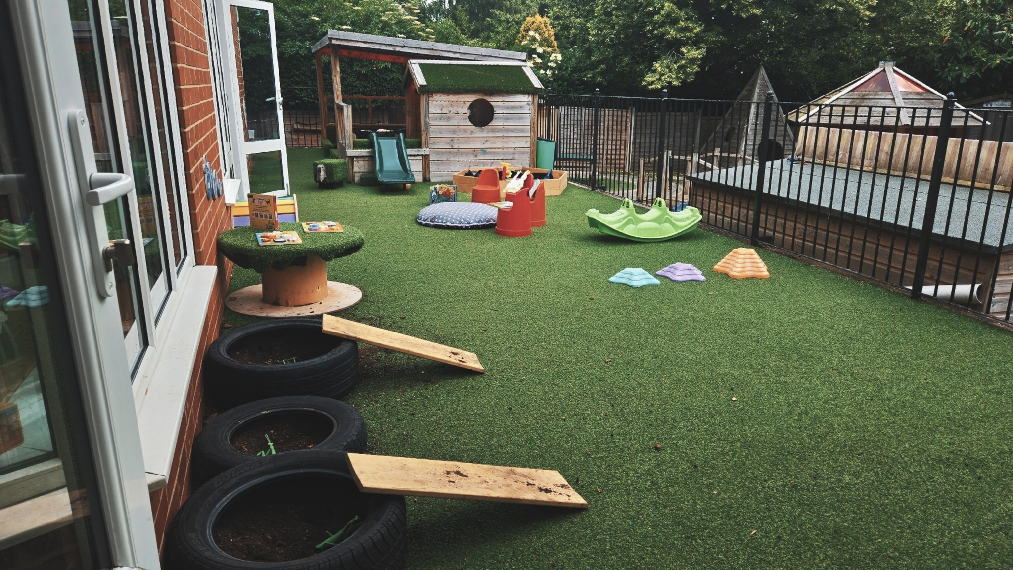 Green astroturf with tyres, balance beams and a wooden structure with slide at Partou Magic Garden Nursery in Moortown, Leeds