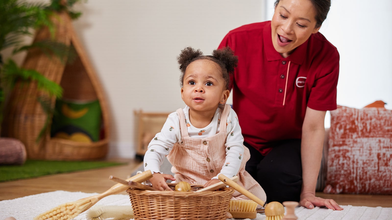 Young child at on the floor with female nursery worker, with a basket of toys