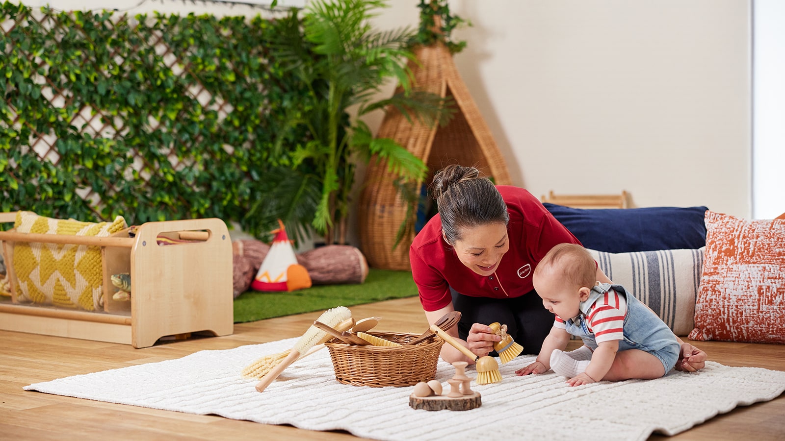 Female nursery worker leaning down with a baby playing with various objects
