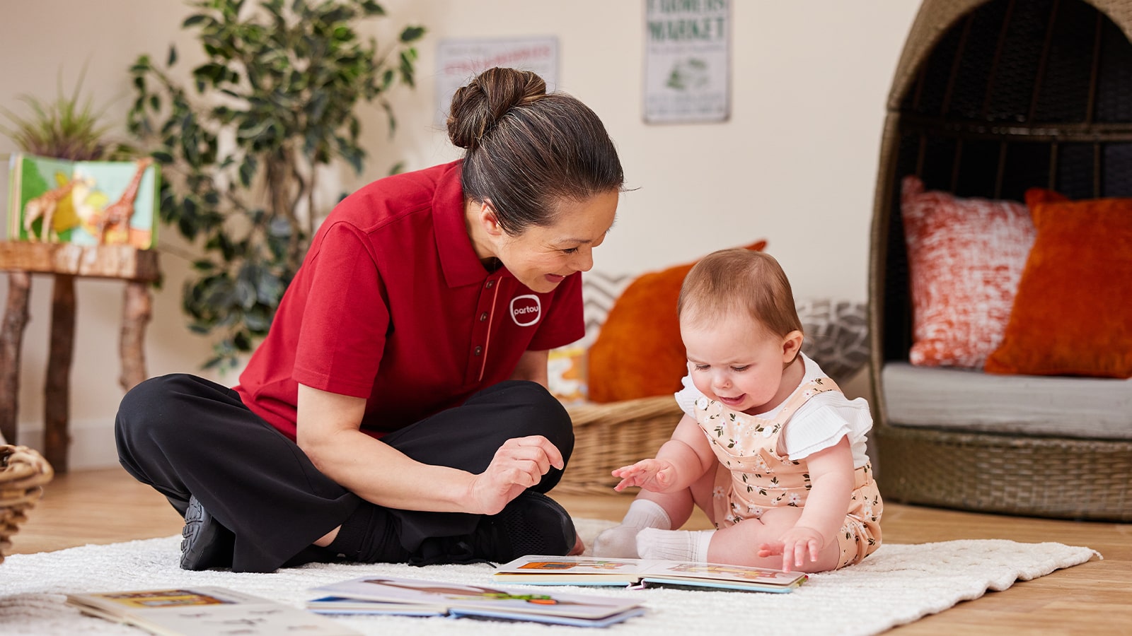 Female nursery worker, sitting down with a baby reading books