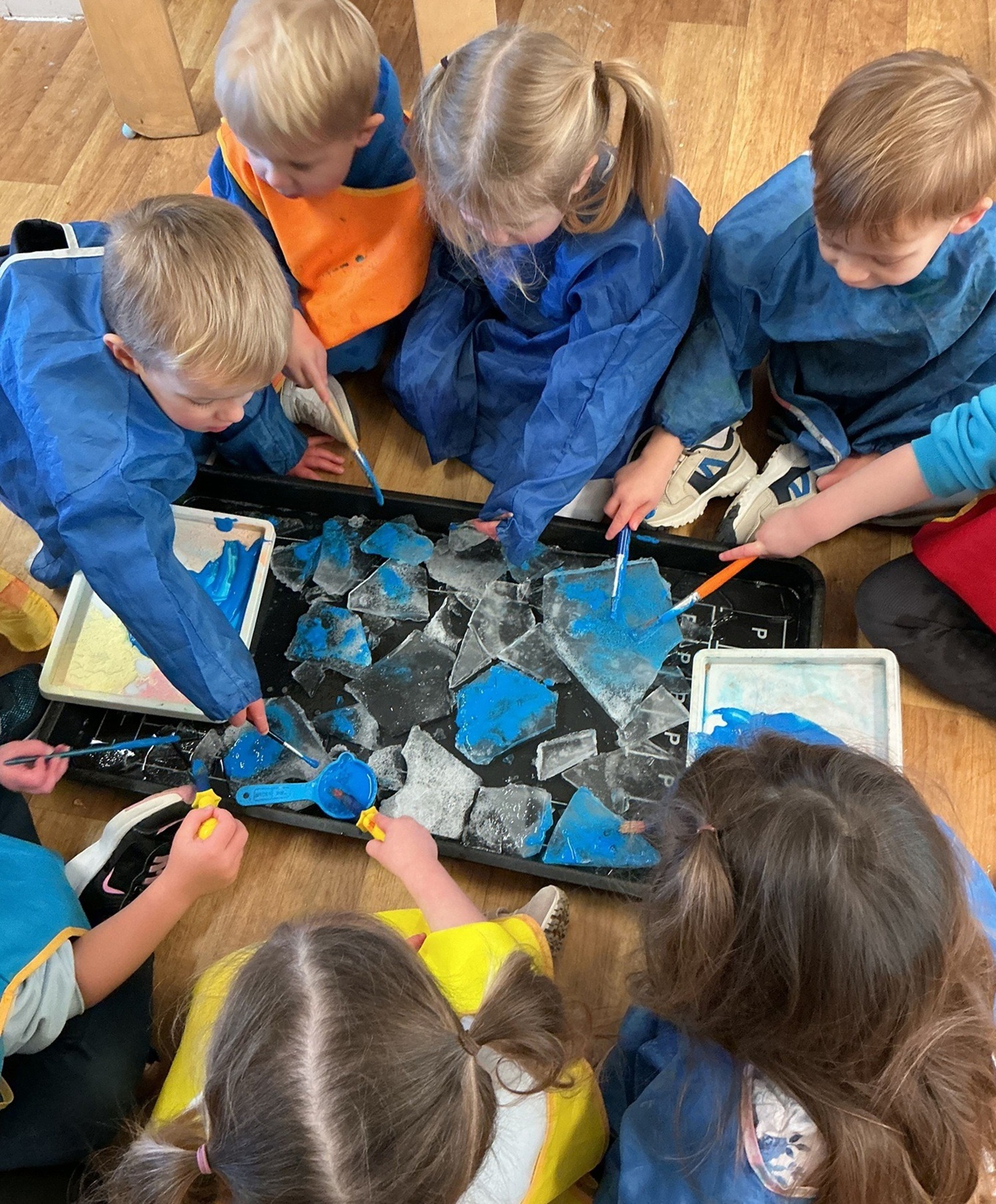 Overhead view of children dressed in blue painting aprons creating blue artwork at Partou Willowdene Day Nursery
