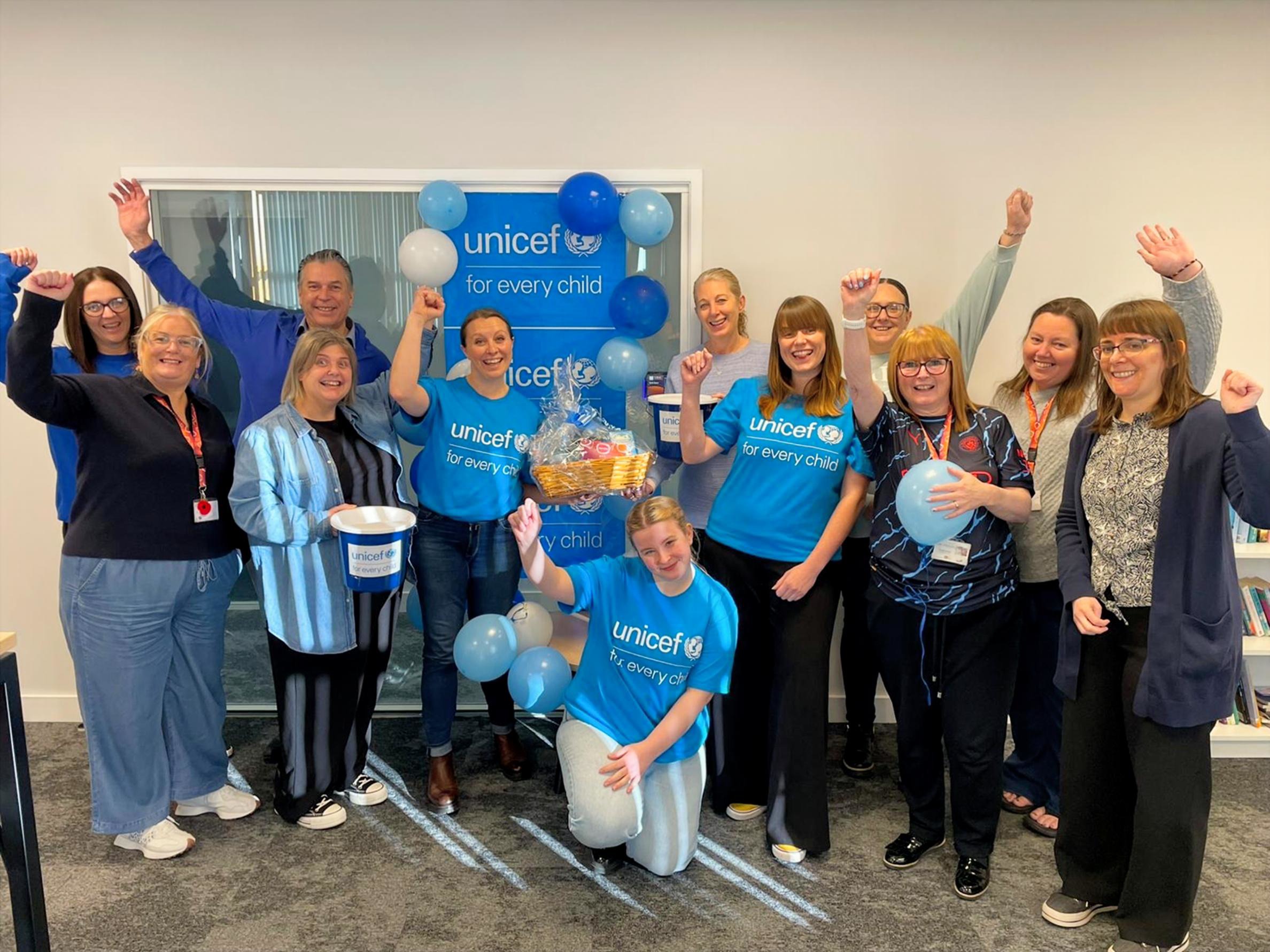 Team members at Partou dressed in blue stood in front of a UNICEF banner with blue balloons