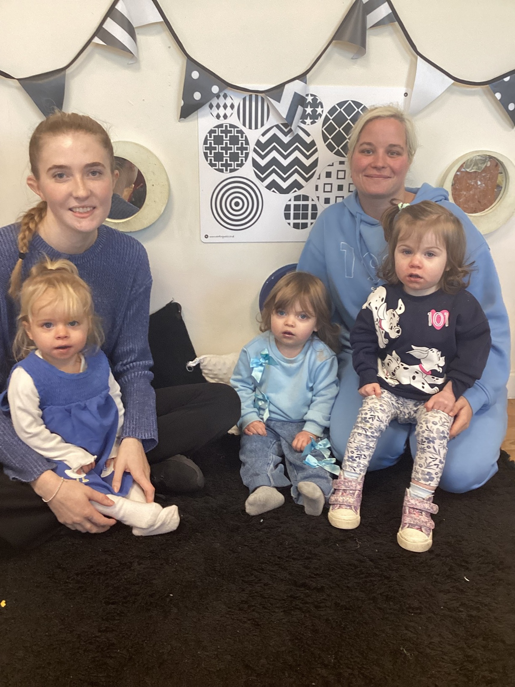 Nursery practitioners and children at Partou Little People in Burnley dressed in blue sat down and smiling
