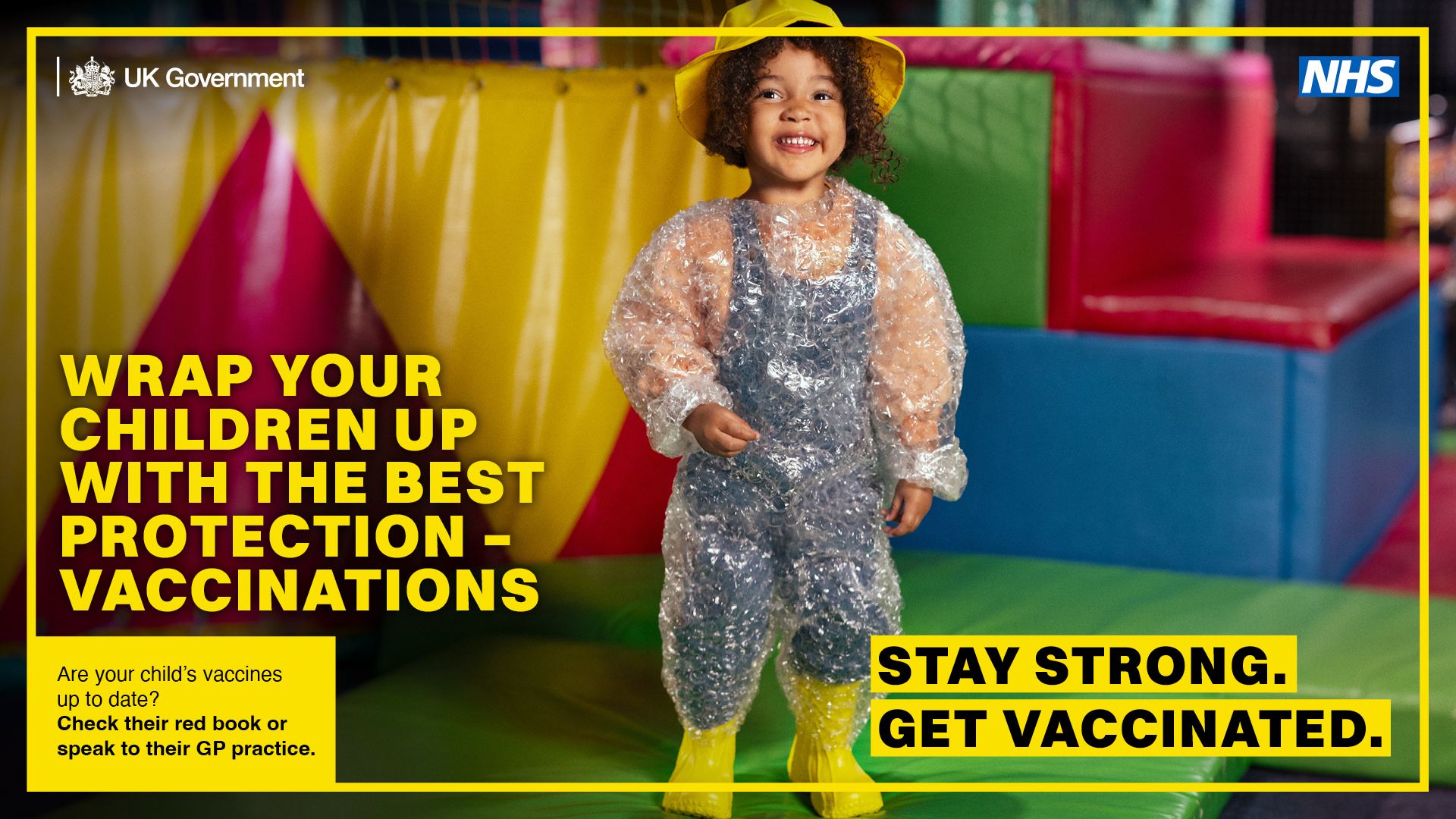 A child wearing waterproof clothing stands in a colourful play area alongside NHS and UK Government messaging promoting childhood vaccinations, with the text “Stay strong. Get vaccinated.”