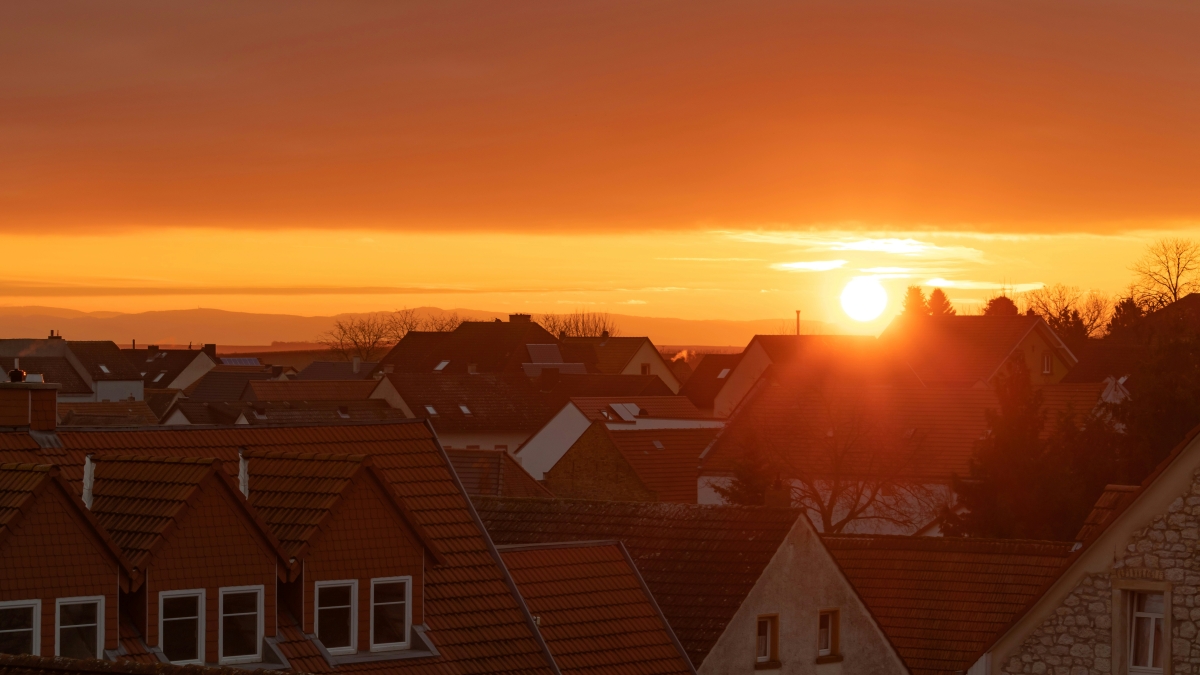 Sunset over a quiet suburban neighbourhood with warm orange light falling across rooftops and distant hills; a calm visual to support guidance for families as the clocks go forwards 2026. Photo by Andrew D on Unsplash.
