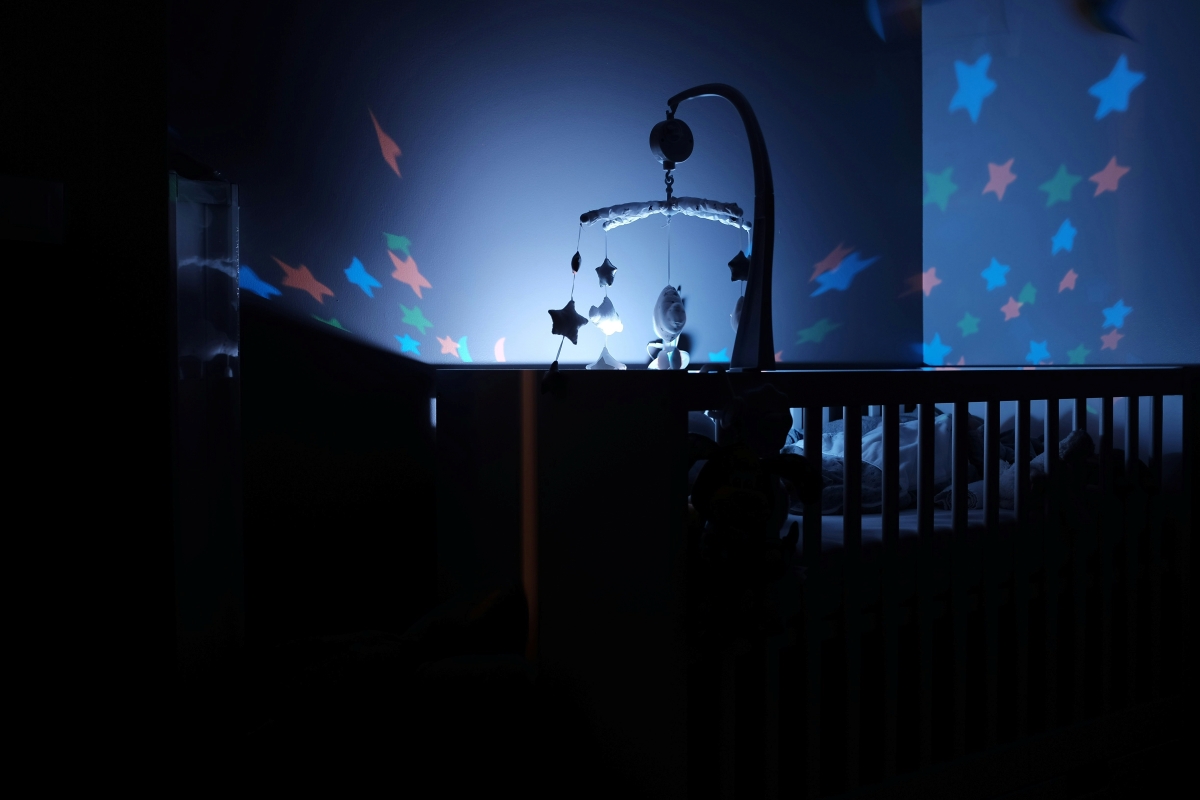 Dimly lit nursery with a crib and colourful star projections on the walls, creating a calm bedtime atmosphere; a gentle visual for supporting families as the clocks go forwards 2026. Photo by Bastien Jaillot on Unsplash.