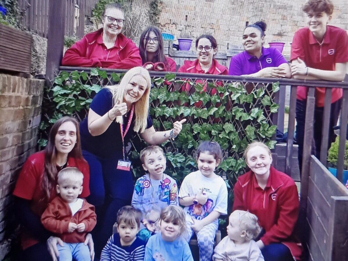Nursery team members and young children at Partou Sycamore House Day Nursery & Pre‑school pose together in an outdoor play area during an Ofsted celebration.