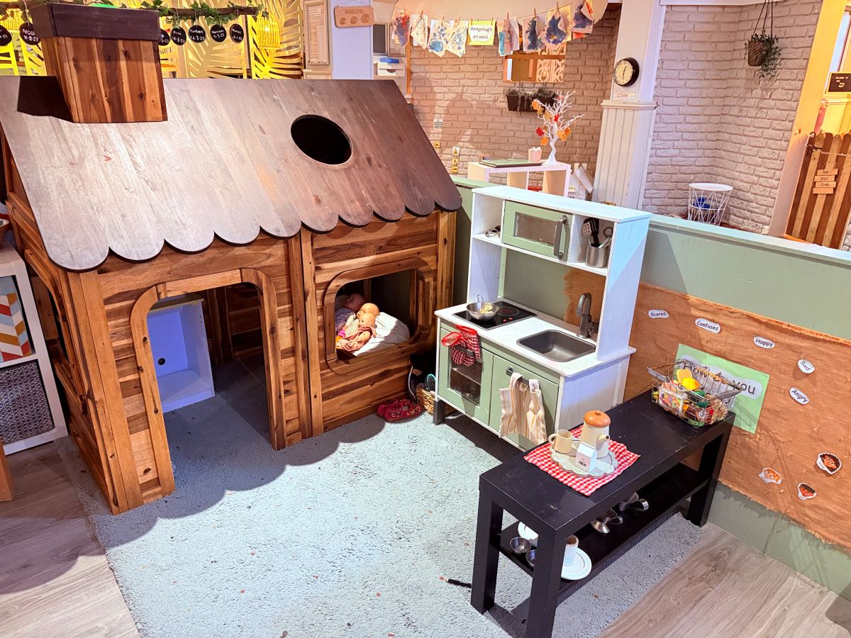 Home‑corner play area at Partou The Railway Euxton Day Nursery with wooden playhouse, toy kitchen and role‑play resources