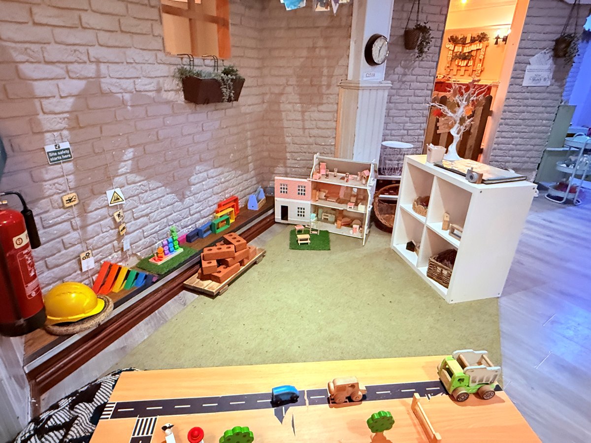 Small‑world play area at Partou The Railway Euxton Day Nursery with dollhouse, construction toys and road‑themed activity table