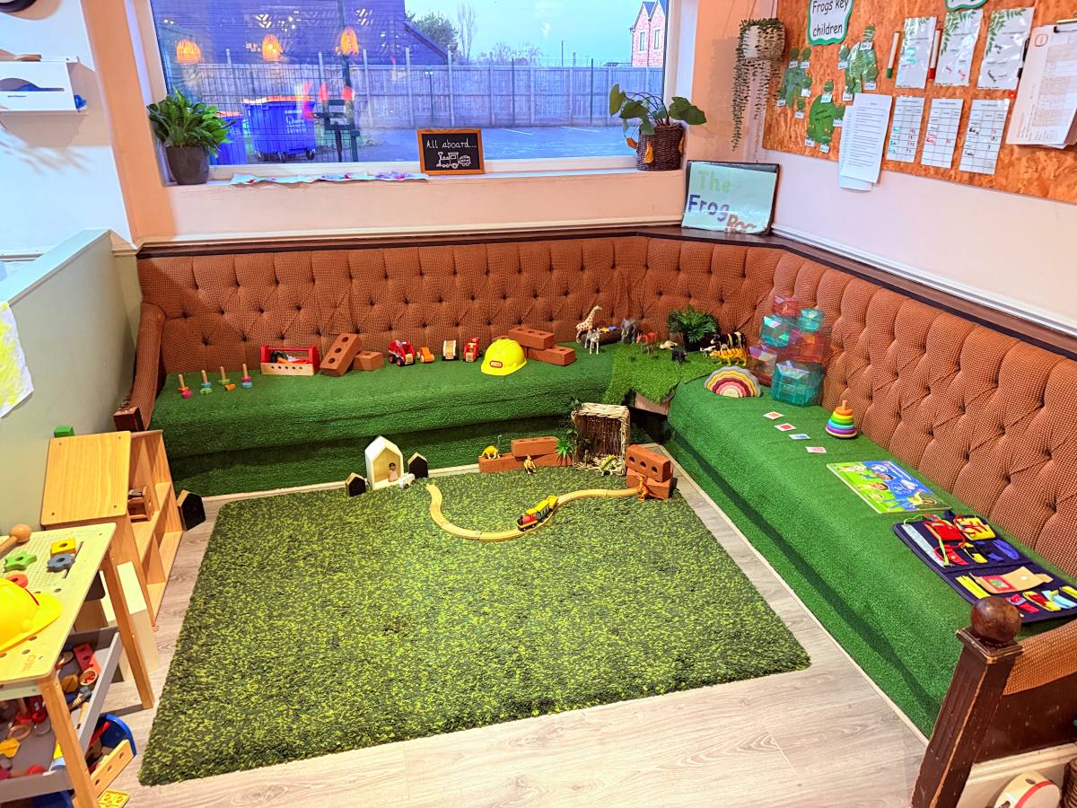 Small‑world play area at Partou The Railway Euxton Day Nursery with toy animals, building blocks and a grassy‑themed seating space