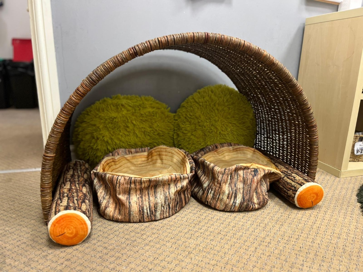 A cosy woodland‑themed rest area at Partou Chorley Day Nursery & Pre‑School, featuring a woven arch canopy with log‑style cushions and soft green moss‑like pillows, creating a calm, nature‑inspired space for quiet time and relaxation.