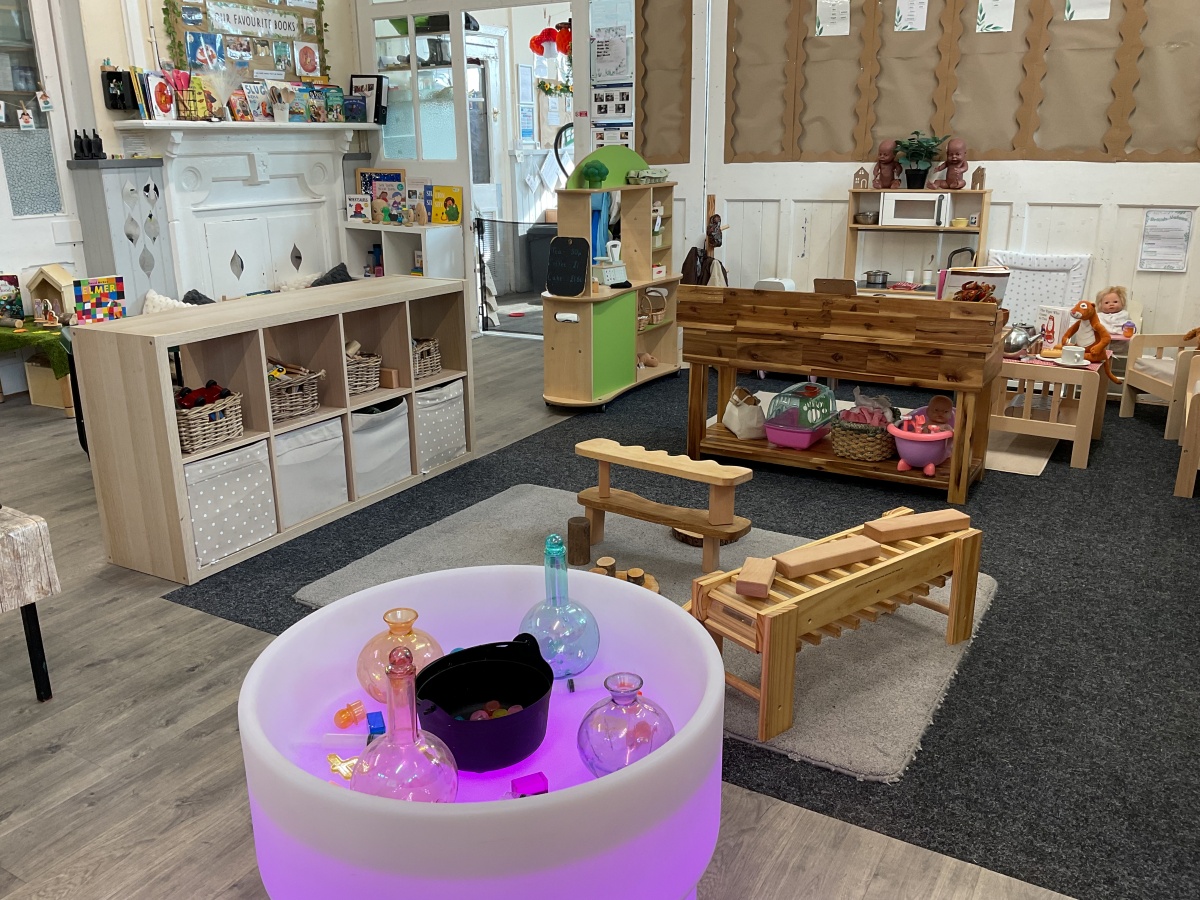 Bright toddler sensory play area at Partou Parbold Day Nursery & Pre-school, featuring natural wood furniture, a black and white geometric rug, pastel sensory balls, shimmering silver and rainbow sensory resources, and colourful red, blue, yellow, purple and green exploration materials. The warm, inviting learning environment encourages curiosity, imaginative play and early childhood development.