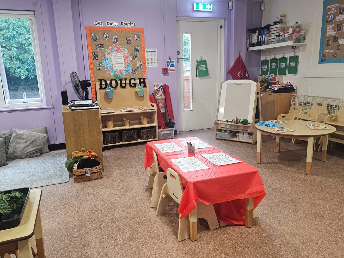 Creative learning classroom at Partou Manchester Airport Day Nursery & Pre-School featuring soft lavender walls, natural wooden furniture, a red activity table, easel painting station and inviting early years learning resources.