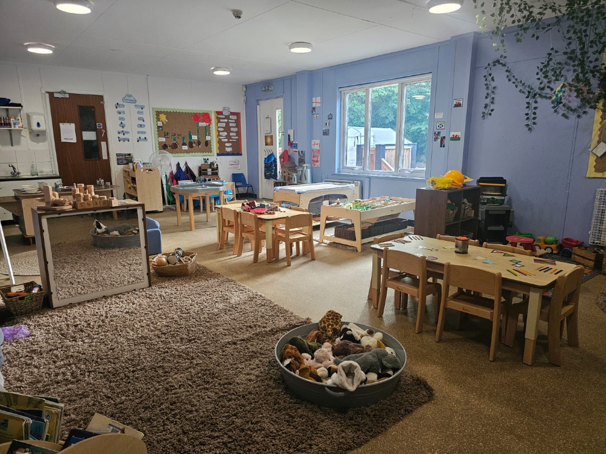 Spacious nursery classroom at Partou Manchester Airport Day Nursery & Pre-School featuring soft blue walls, natural wooden furniture, sensory play tables, creative activity stations, cosy textured rugs, soft toy resources and child-led early years learning environments.