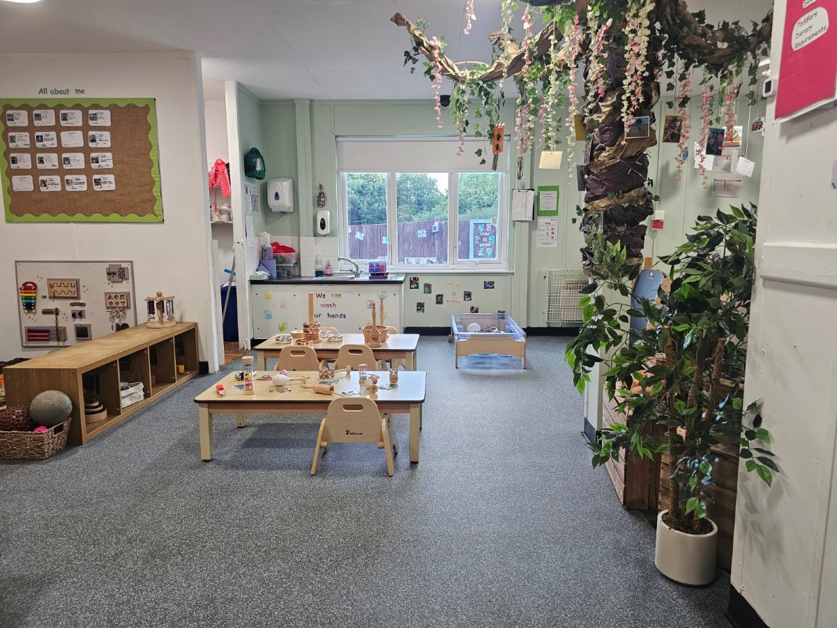 Nature-inspired nursery classroom at Partou Manchester Airport Day Nursery & Pre-School featuring a large decorative indoor tree with green foliage, natural wooden furniture, sensory play tables, open-ended learning resources and bright early years activity spaces.
