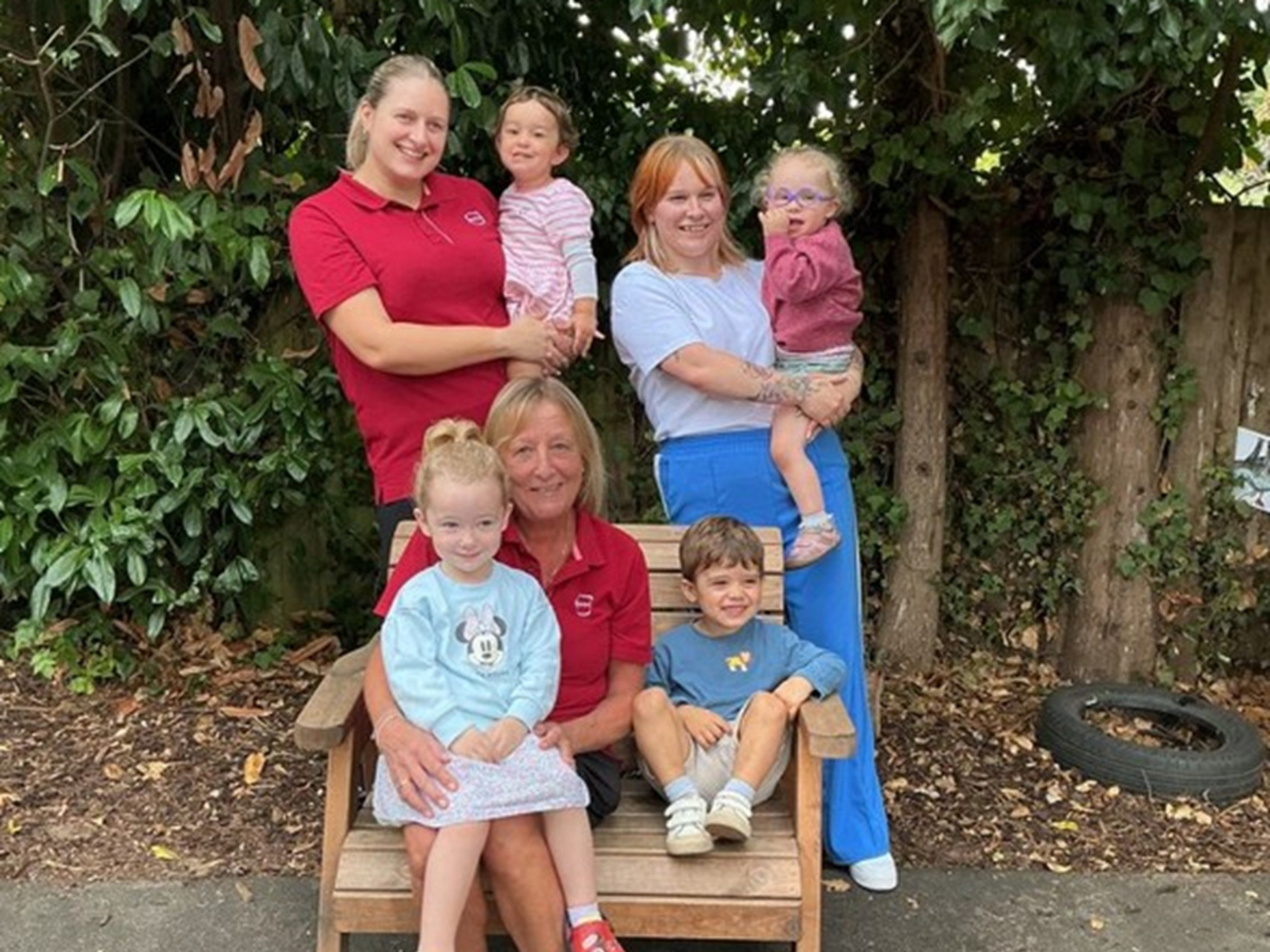 Become a partou level 3 nursery practitioner 8 Children and nursery staff from partou westfields day nursery & pre-school in cheltenham celebrating a positive ofsted inspection result outdoors, with red and blue clothing against a green leafy garden backdrop, highlighting the nursery