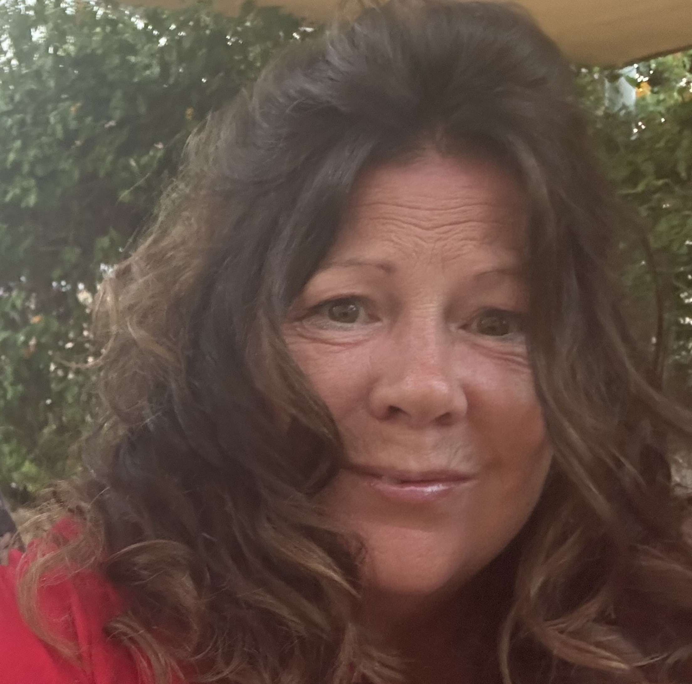 Image of brunette, curly haired Dr Karen Boardman - Partou Group SEND and Inclusion Lead, smiling and wearing a red blouse whilst standing in front of a large tree.